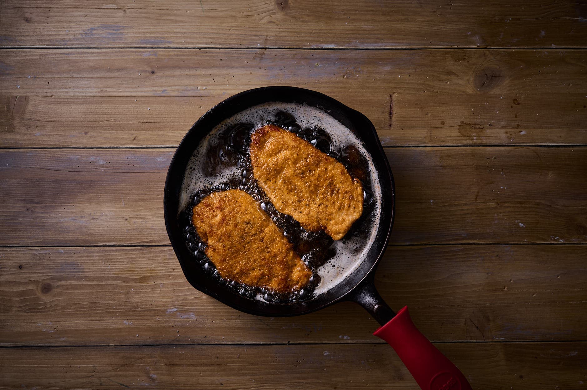  Fried Picatta Milanese in a skillet, as it approaches a golden brown color in bubbling oil and butter. 