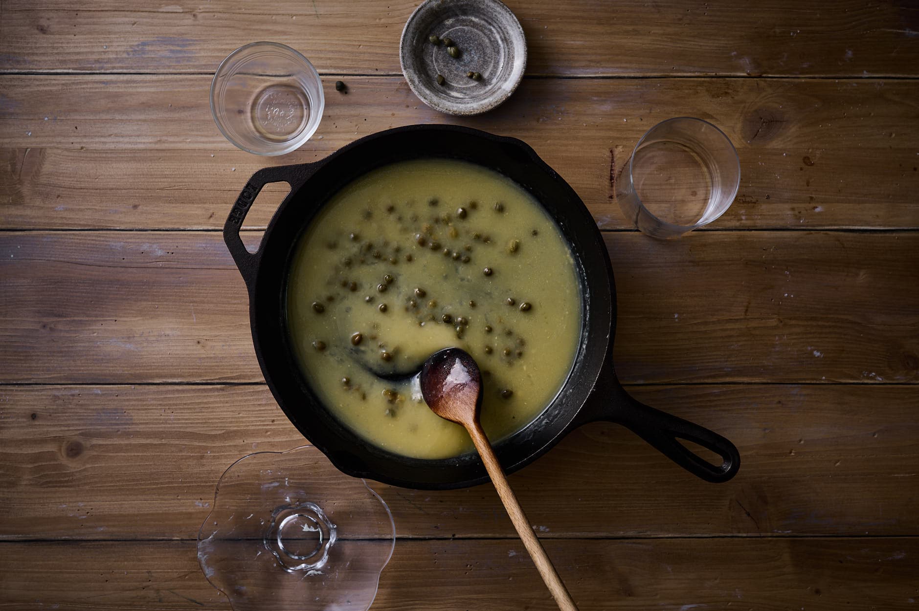 zesty sauce made from lemons, capers, and butter in a skillet on a distressed wooden table for Picatta milanese.