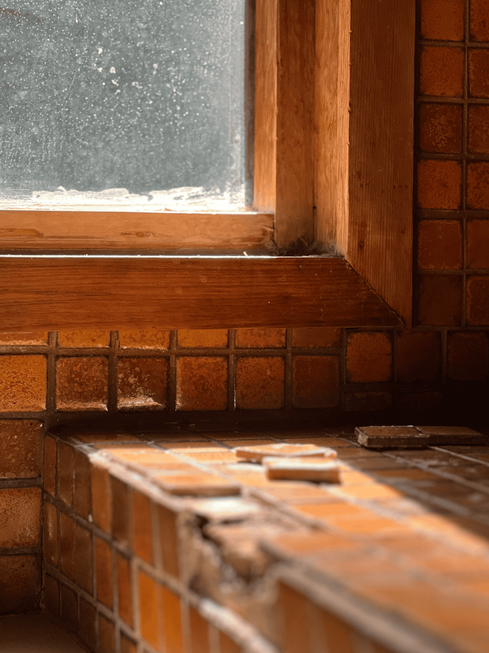 crumbling beige tile and a fogged failed window in a bathroom bench seat.