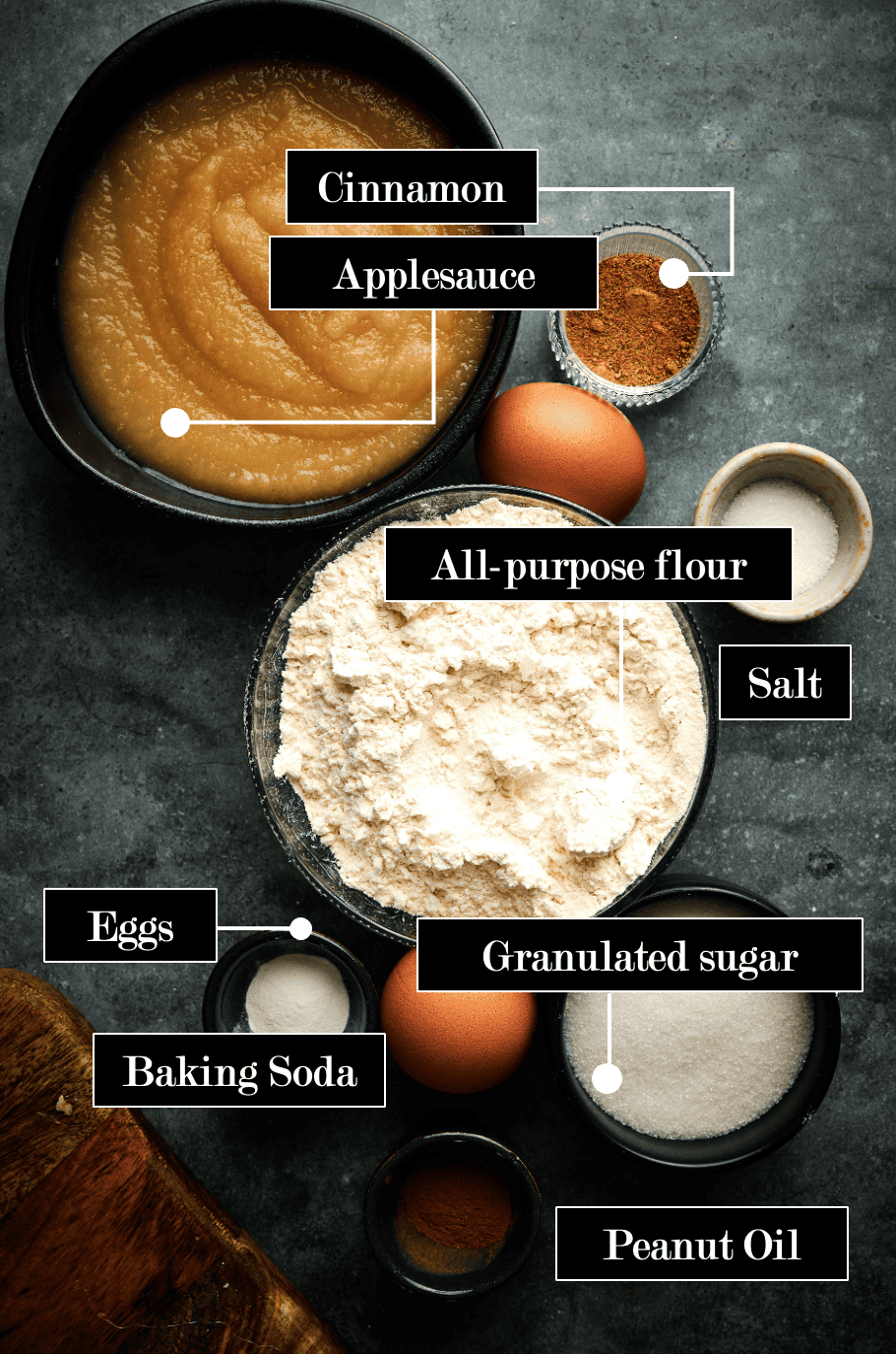 Key ingredients to make applesauce fritters including bowls of; flour, salt, cinnamon, baking soda, eggs, oil, and sugar. 