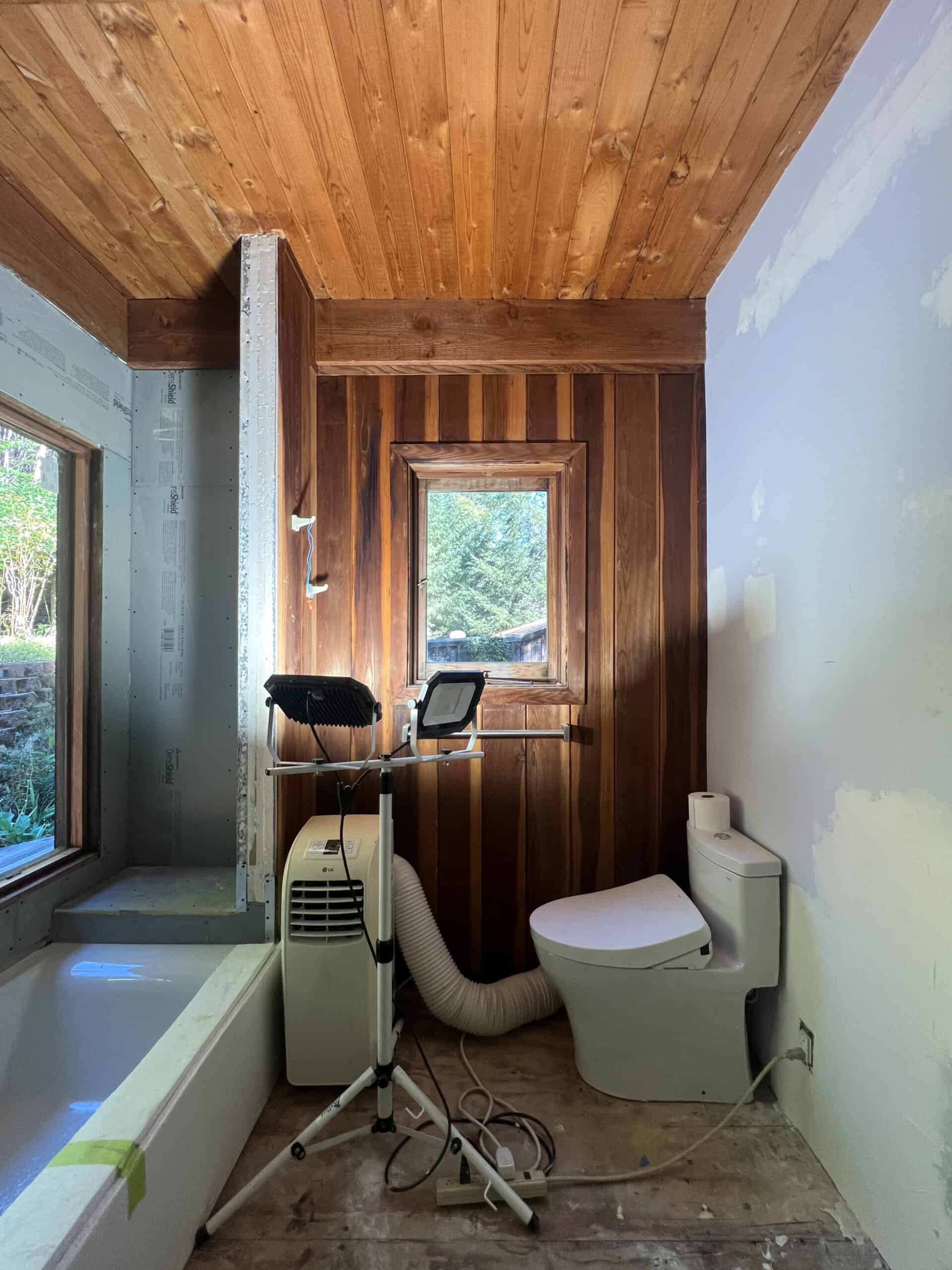 a fully gutted moody bath with patched dry wall, removed subfloor, and a bath installed with lights. 