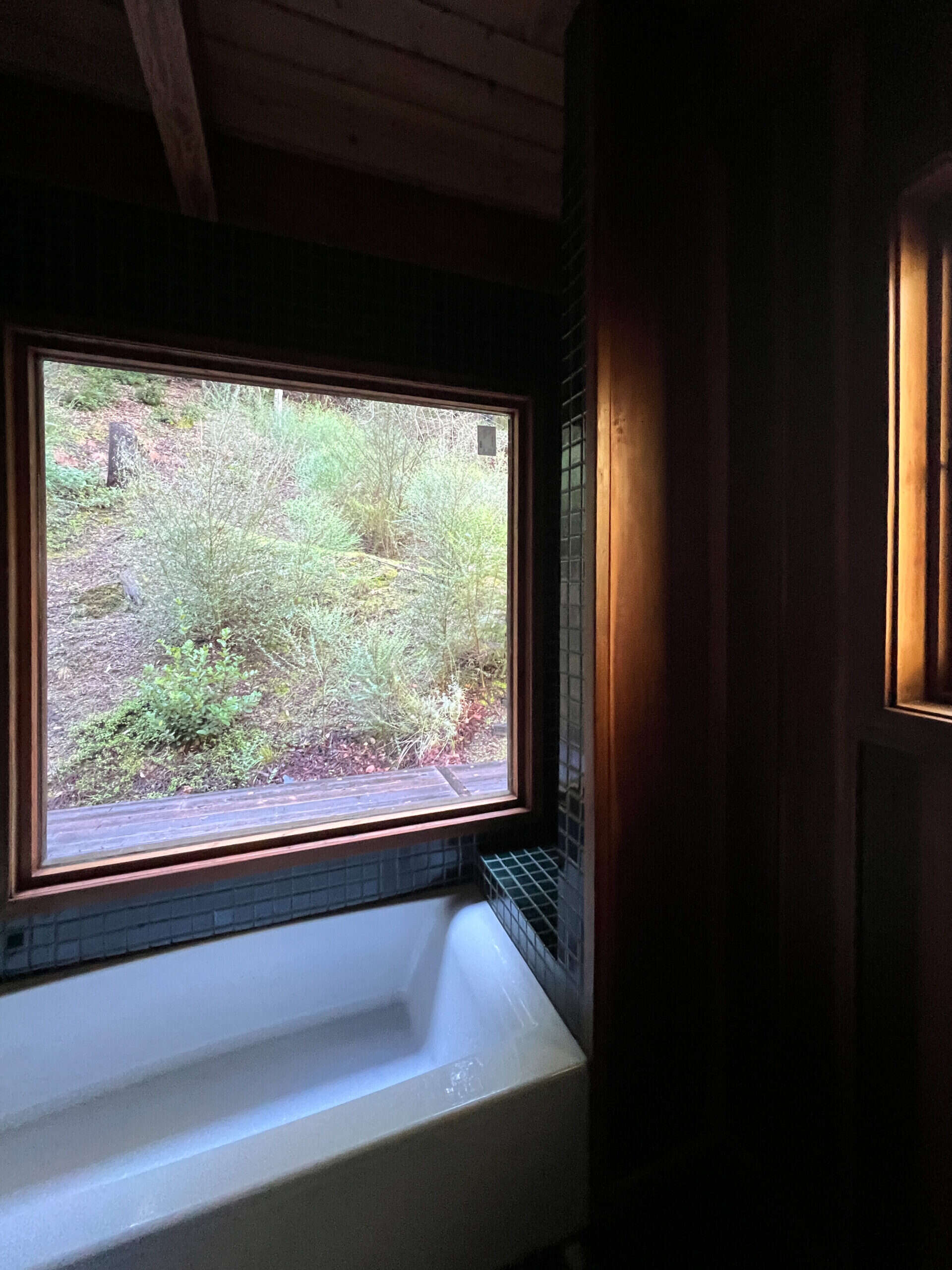 picture frame, redwood window over a white bathtub, reflecting the warm afternoon glow of the window at a slightly angled pov.