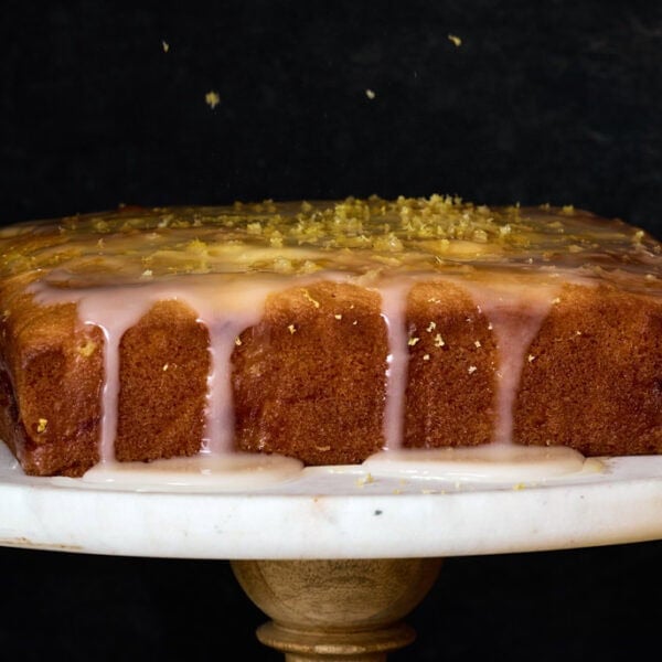 freshly served lemon curd cake with lemon zest in a gorgeous dark room a top a cake tray.
