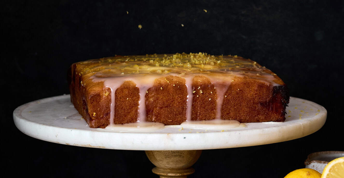 freshly served lemon curd cake with lemon zest in a gorgeous dark room a top a cake tray.