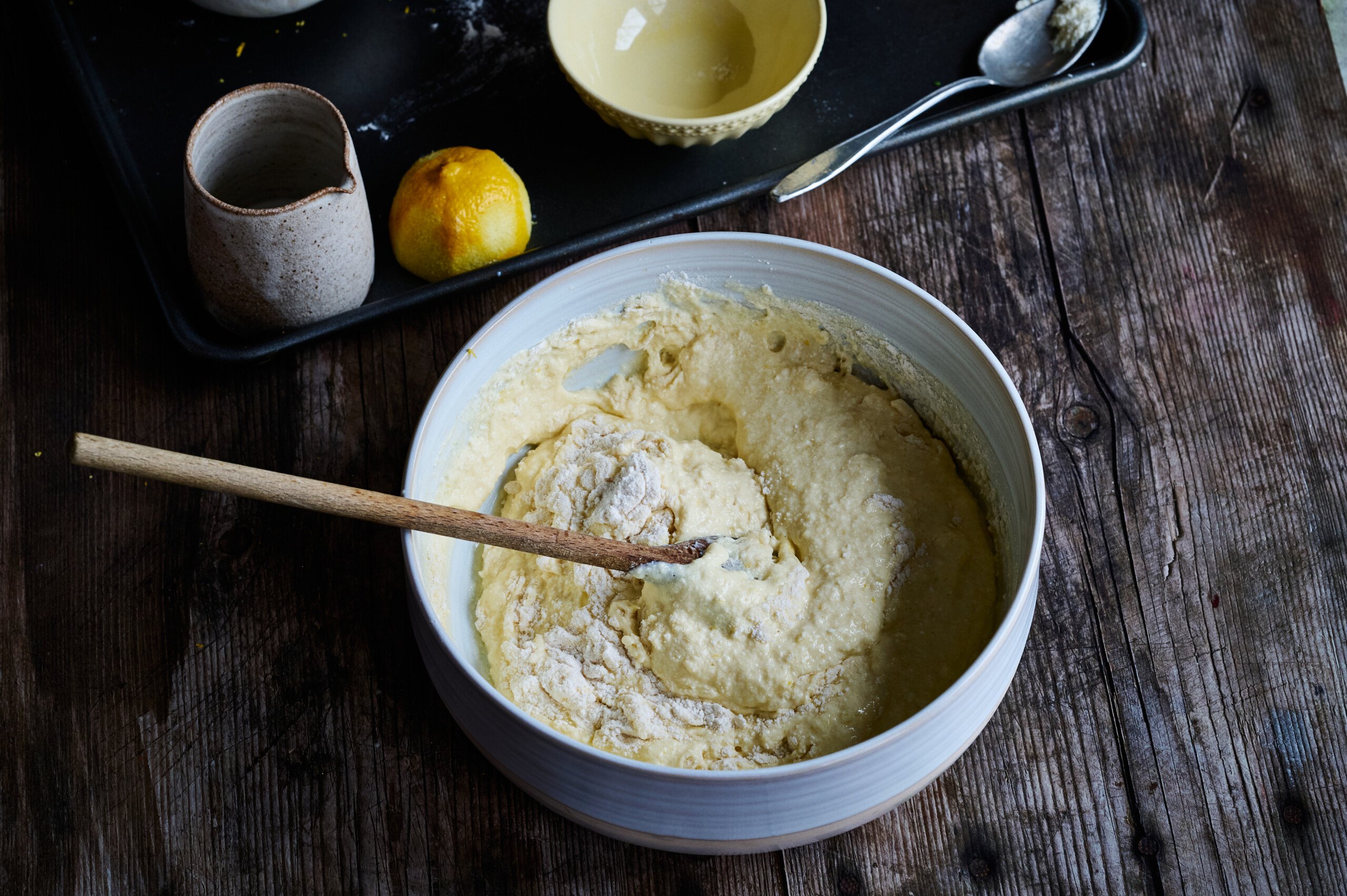 Dry ingredients folding into wet ingredients in a large white mixing bowl for lemon ricotta panackes,