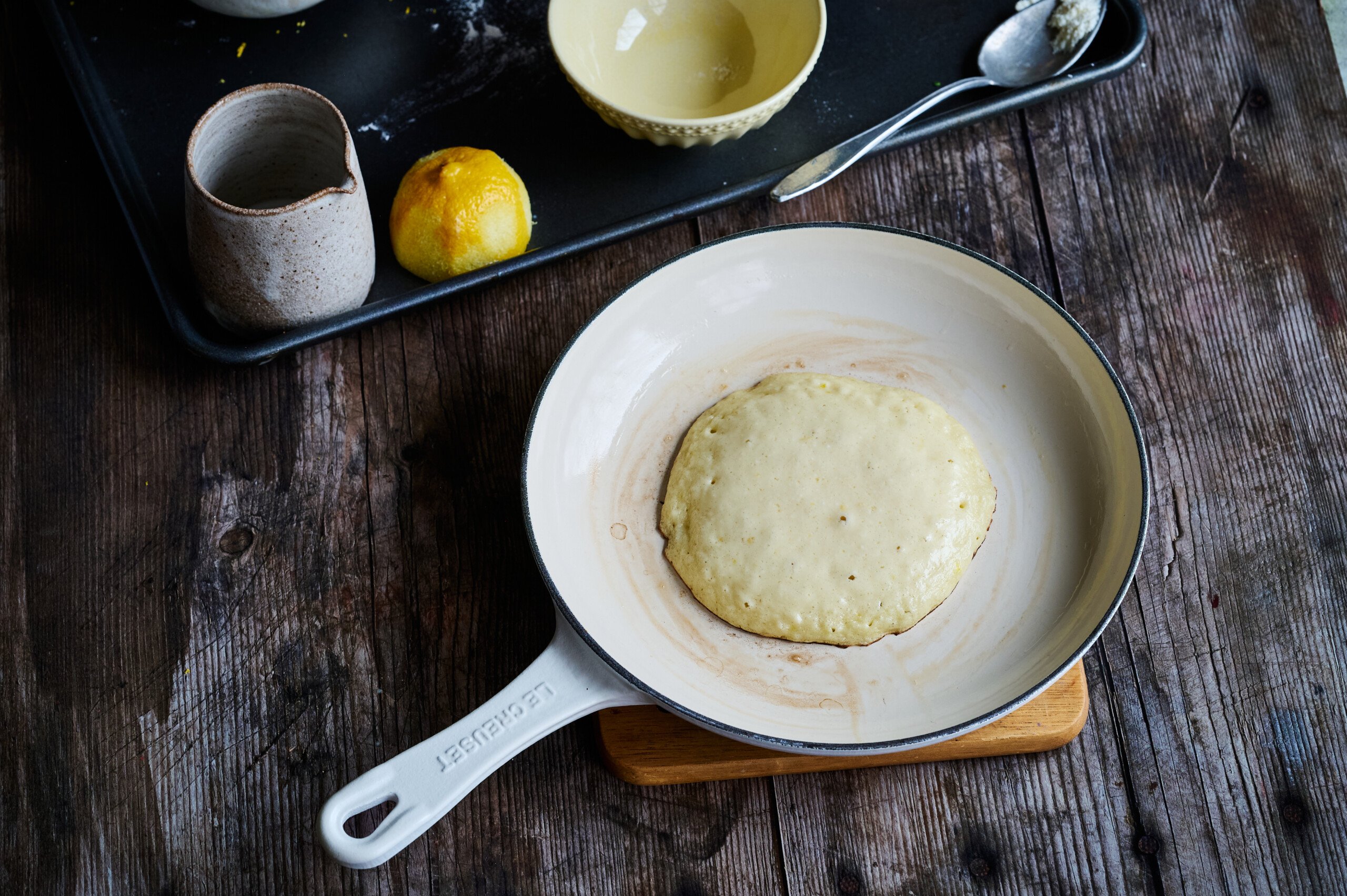 cooking lemon ricotta pancakes in a white pan, lightly cooked with the wet side up.