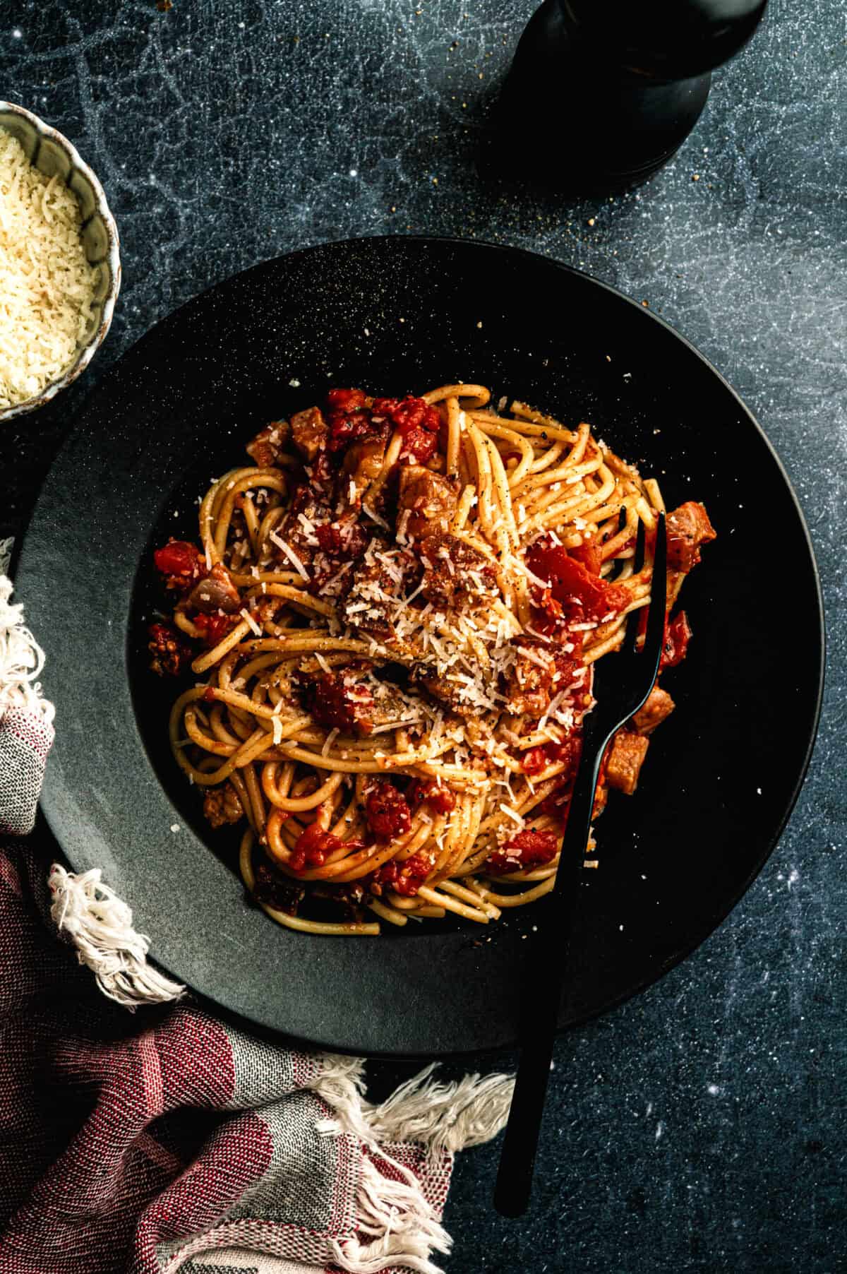 Amatriciana pasta dish in a black bowl with fresh tomatoes, pecorino cheese, and a light dusting of pepper.