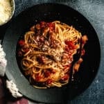 Amatriciana pasta dish in a black bowl with fresh tomatoes, pecorino cheese, and a light dusting of pepper.