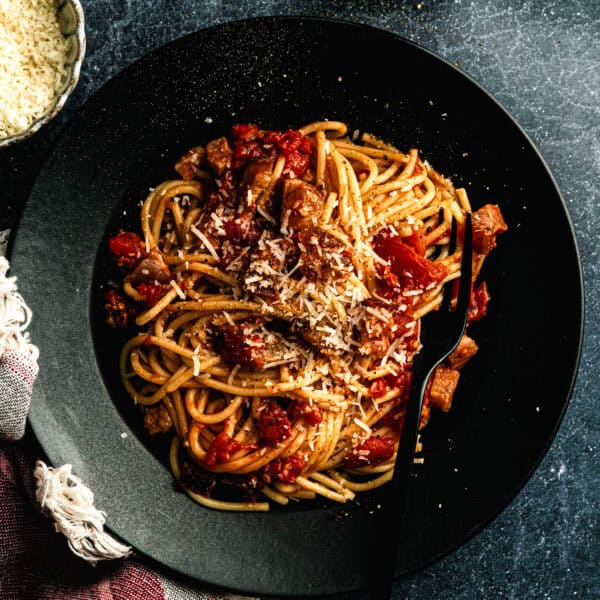 Amatriciana pasta dish in a black bowl with fresh tomatoes, pecorino cheese, and a light dusting of pepper.
