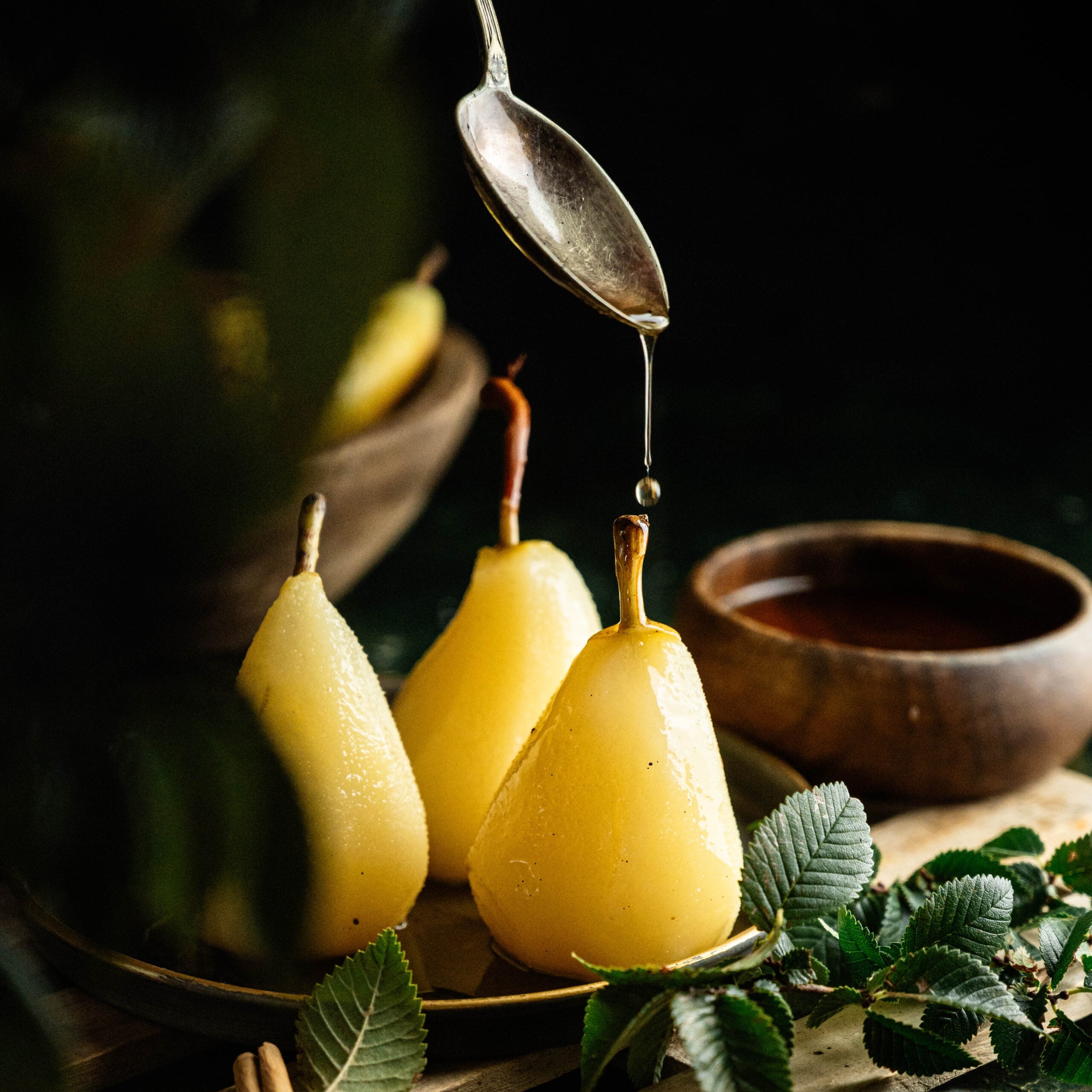 Easy poached pears recipe served with spiced poaching syrup and fresh fruit. on a table with leaves.