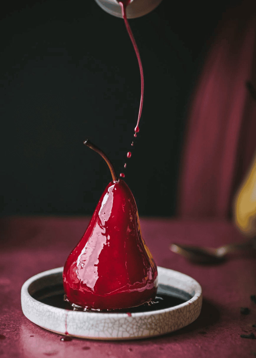 Poached pear made with red win on a table drizzling red wine a top.